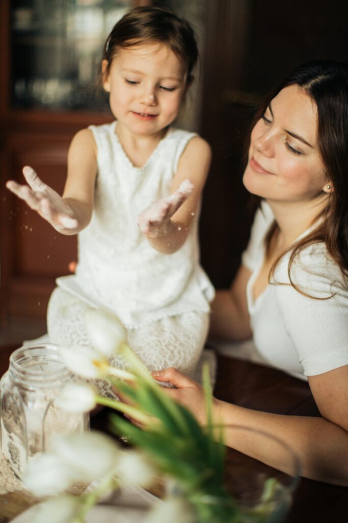A cheerful mother and daughter enjoying a playful moment with flour indoors.