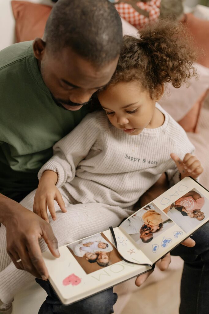 Black father and daughter enjoying a bonding moment with a photo album at home indoors.